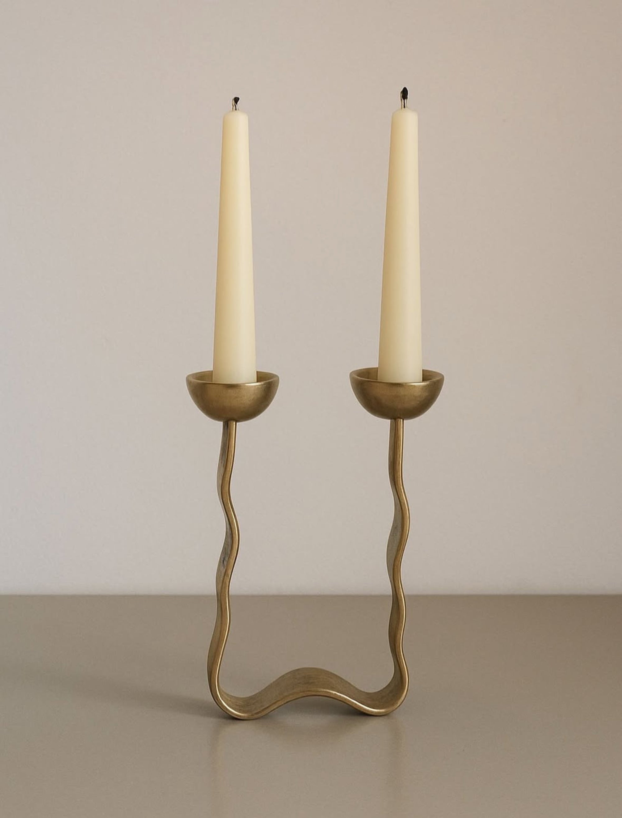 Brass candle holder with two white candles on a beige background